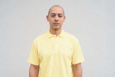 Saçları kazınmış, sarı polo tişörtlü yakışıklı bir İtalyan 'ın stüdyo portresi. Tarafsız beyaz bir duvarın önünde fotokopi alanı ile duruyor. Temiz, izole kesilmiş görünüm.