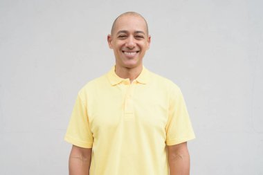 Yakışıklı, olgun, kafası tıraşlı, sarı polo tişört giyen, fotokopi alanı olan tarafsız beyaz bir duvarın önünde duran mutlu bir İtalyan 'ın stüdyo portresi..