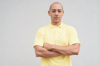 Saçları kazınmış, sarı polo tişörtlü yakışıklı bir İtalyan 'ın stüdyo portresi. Tarafsız beyaz bir duvarın önünde fotokopi alanı ile duruyor. Temiz, izole kesilmiş görünüm.
