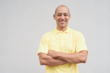 Yakışıklı, olgun, kafası tıraşlı, sarı polo tişört giyen, fotokopi alanı olan tarafsız beyaz bir duvarın önünde duran mutlu bir İtalyan 'ın stüdyo portresi..