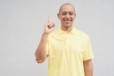 Saçları kazınmış, sarı polo tişörtlü yakışıklı bir İtalyan 'ın stüdyo portresi. Tarafsız beyaz bir duvarın önünde fotokopi alanı ile duruyor. Temiz, izole kesilmiş görünüm.