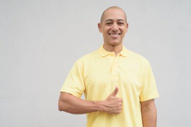Yakışıklı, olgun, kafası tıraşlı, sarı polo tişört giyen, fotokopi alanı olan tarafsız beyaz bir duvarın önünde duran mutlu bir İtalyan 'ın stüdyo portresi..