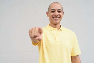 Yakışıklı, olgun, kafası tıraşlı, sarı polo tişört giyen, fotokopi alanı olan tarafsız beyaz bir duvarın önünde duran mutlu bir İtalyan 'ın stüdyo portresi..