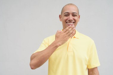 Yakışıklı, olgun, kafası tıraşlı, sarı polo tişört giyen, fotokopi alanı olan tarafsız beyaz bir duvarın önünde duran mutlu bir İtalyan 'ın stüdyo portresi..