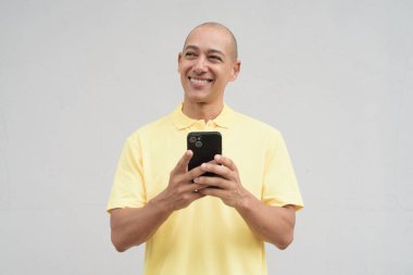 Yakışıklı, olgun, kafası tıraşlı, sarı polo tişört giyen, fotokopi alanı olan tarafsız beyaz bir duvarın önünde duran mutlu bir İtalyan 'ın stüdyo portresi..