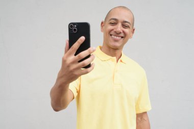 Yakışıklı, olgun, kafası tıraşlı, sarı polo tişört giyen, fotokopi alanı olan tarafsız beyaz bir duvarın önünde duran mutlu bir İtalyan 'ın stüdyo portresi..