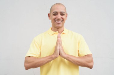 Yakışıklı, olgun, kafası tıraşlı, sarı polo tişört giyen, fotokopi alanı olan tarafsız beyaz bir duvarın önünde duran mutlu bir İtalyan 'ın stüdyo portresi..