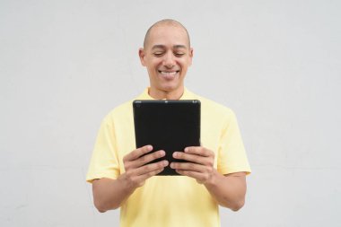 Yakışıklı, olgun, kafası tıraşlı, sarı polo tişört giyen, fotokopi alanı olan tarafsız beyaz bir duvarın önünde duran mutlu bir İtalyan 'ın stüdyo portresi..