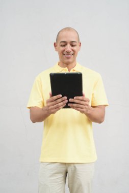 Yakışıklı, olgun, kafası tıraşlı, sarı polo tişört giyen, fotokopi alanı olan tarafsız beyaz bir duvarın önünde duran mutlu bir İtalyan 'ın stüdyo portresi..