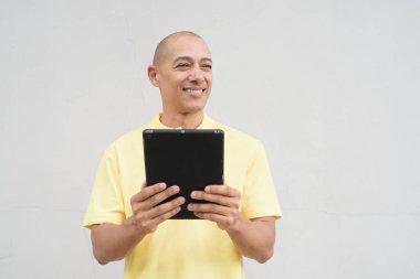 Yakışıklı, olgun, kafası tıraşlı, sarı polo tişört giyen, fotokopi alanı olan tarafsız beyaz bir duvarın önünde duran mutlu bir İtalyan 'ın stüdyo portresi..