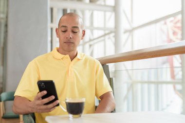 Kendine güveni tam bir İtalyan kel adam şık bir kafede oturmuş kahve molası verirken telefonla konuşuyor. Modern yaşam tarzı ve iş konsepti.