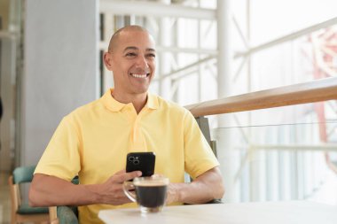 Kendine güveni tam bir İtalyan kel adam şık bir kafede oturmuş kahve molası verirken telefonla konuşuyor. Modern yaşam tarzı ve iş konsepti.