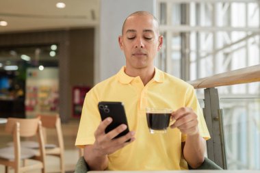 Kendine güveni tam bir İtalyan kel adam şık bir kafede oturmuş kahve molası verirken telefonla konuşuyor. Modern yaşam tarzı ve iş konsepti.