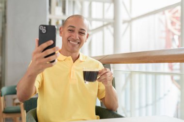 Kendine güveni tam bir İtalyan kel adam şık bir kafede oturmuş kahve molası verirken telefonla konuşuyor. Modern yaşam tarzı ve iş konsepti.