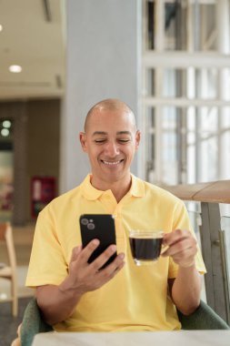 Kendine güveni tam bir İtalyan kel adam şık bir kafede oturmuş kahve molası verirken telefonla konuşuyor. Modern yaşam tarzı ve iş konsepti.