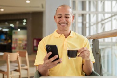 Kendine güveni tam bir İtalyan kel adam şık bir kafede oturmuş kahve molası verirken telefonla konuşuyor. Modern yaşam tarzı ve iş konsepti.