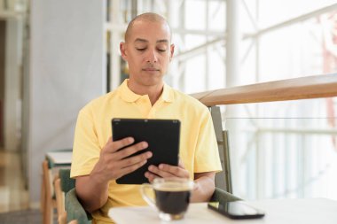 Gündüzleri dijital tablet bilgisayar kullanarak kahve molası verirken şık bir kafede oturan kendinden emin, kel bir İtalyan. Modern yaşam tarzı ve iş konsepti.