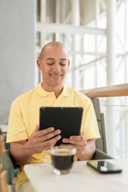 Gündüzleri dijital tablet bilgisayar kullanarak kahve molası verirken şık bir kafede oturan kendinden emin, kel bir İtalyan. Modern yaşam tarzı ve iş konsepti.