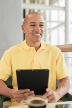 Gündüzleri dijital tablet bilgisayar kullanarak kahve molası verirken şık bir kafede oturan kendinden emin, kel bir İtalyan. Modern yaşam tarzı ve iş konsepti.