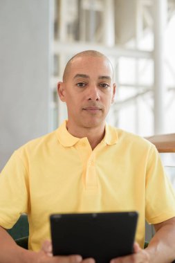 Gündüzleri dijital tablet bilgisayar kullanarak kahve molası verirken şık bir kafede oturan kendinden emin, kel bir İtalyan. Modern yaşam tarzı ve iş konsepti.