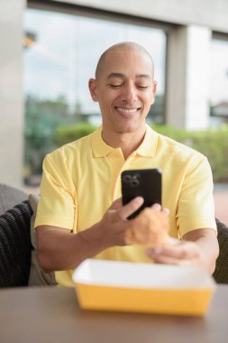 Orta yaşlı İspanyol bir adamın portresi açık havada oturuyor ve öğle yemeği sırasında kızarmış tavuk yiyor, açık hava restoranlarında rahat bir hayat sürüyor ve telefon kullanıyor..