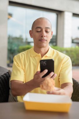 Orta yaşlı İspanyol bir adamın portresi açık havada oturuyor ve öğle yemeği sırasında kızarmış tavuk yiyor, açık hava restoranlarında rahat bir hayat sürüyor ve telefon kullanıyor..