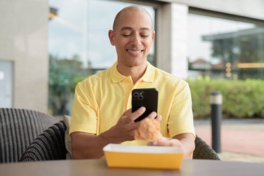 Orta yaşlı İspanyol bir adamın portresi açık havada oturuyor ve öğle yemeği sırasında kızarmış tavuk yiyor, açık hava restoranlarında rahat bir hayat sürüyor ve telefon kullanıyor..