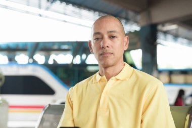 Açık hava otobüs durağında oturan, kameraya bakarken ulaşımı bekleyen olgun, kel bir İspanyol. Tayland 'da seyahat, seyahat ve toplu taşıma kavramı.