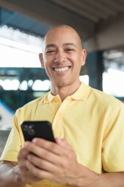 Açık hava otobüs durağında oturan, akıllı telefonuna göz gezdirirken ulaşımı bekleyen olgun, kel bir İspanyol. Tayland 'da seyahat, seyahat ve toplu taşıma kavramı.