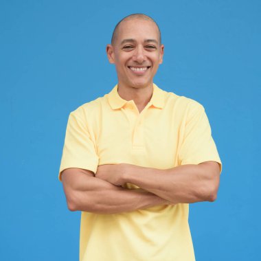 Saçları kazınmış, sarı polo tişörtlü yakışıklı bir İtalyan 'ın stüdyo portresi. Tarafsız, mavi duvarın önünde duruyor. Temiz, izole kesilmiş görünüm.