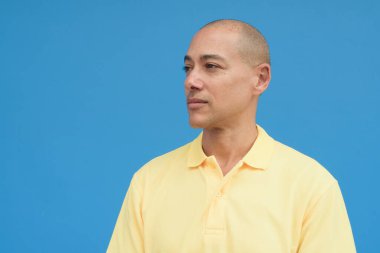 Saçları kazınmış, sarı polo tişörtlü yakışıklı bir İtalyan 'ın stüdyo portresi. Tarafsız, mavi duvarın önünde duruyor. Temiz, izole kesilmiş görünüm.