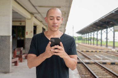 Siyah tişörtlü, olgun, kel bir İspanyol turistin portresi tren istasyonunda telefonla Tayland 'da tren beklerken çekilmiş. Turizm, seyahat ve ulaşım teması.