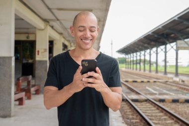 Siyah tişörtlü, olgun, kel bir İspanyol turistin portresi tren istasyonunda telefonla Tayland 'da tren beklerken çekilmiş. Turizm, seyahat ve ulaşım teması.