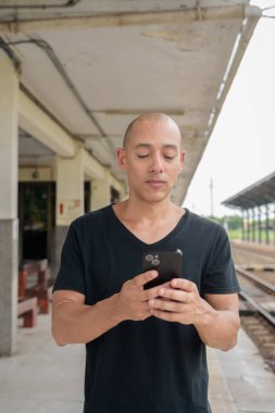 Siyah tişörtlü, olgun, kel bir İspanyol turistin portresi tren istasyonunda telefonla Tayland 'da tren beklerken çekilmiş. Turizm, seyahat ve ulaşım teması.