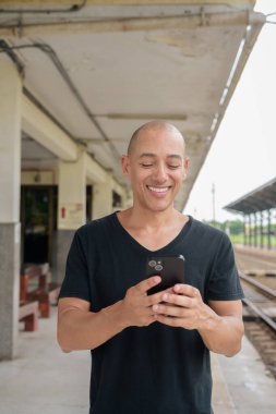 Siyah tişörtlü, olgun, kel bir İspanyol turistin portresi tren istasyonunda telefonla Tayland 'da tren beklerken çekilmiş. Turizm, seyahat ve ulaşım teması.