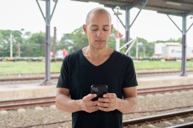 Siyah tişörtlü, olgun, kel bir İspanyol turistin portresi tren istasyonunda telefonla Tayland 'da tren beklerken çekilmiş. Turizm, seyahat ve ulaşım teması.