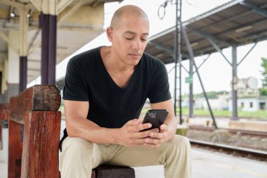 Tayland 'da seyahat ederken tren istasyonunda oturan siyah tişörtlü, olgun, kel bir İspanyol turistin portresi. Turizm, seyahat ve ulaşım teması.