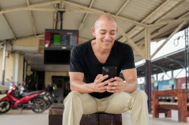 Tayland 'da seyahat ederken tren istasyonunda oturan siyah tişörtlü, olgun, kel bir İspanyol turistin portresi. Turizm, seyahat ve ulaşım teması.