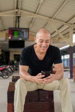 Tayland 'da seyahat ederken tren istasyonunda oturan siyah tişörtlü, olgun, kel bir İspanyol turistin portresi. Turizm, seyahat ve ulaşım teması.