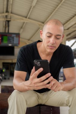 Tayland 'da seyahat ederken tren istasyonunda oturan siyah tişörtlü, olgun, kel bir İspanyol turistin portresi. Turizm, seyahat ve ulaşım teması.