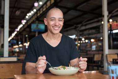 Orta yaşlı, kel, İspanyol bir turistin portresi. Tayland restoranında Tayland eriştesinin tadını çıkarıyor. Yemek yerken gülümsüyor ve yerel mutfağı deneyimliyor..