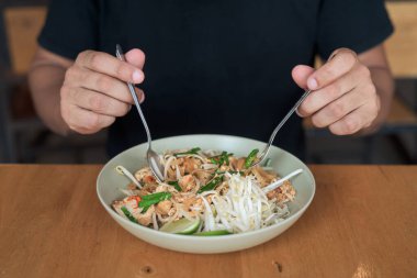 Orta yaşlı, kel, İspanyol bir turistin portresi. Tayland restoranında Tayland eriştesinin tadını çıkarıyor. Yemek yerken gülümsüyor ve yerel mutfağı deneyimliyor..
