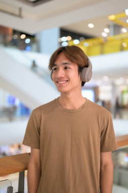 Kulaklıklı yakışıklı Asyalı genç Taylandlı modern yaşam tarzının tadını çıkarıyor müzik dinliyor.