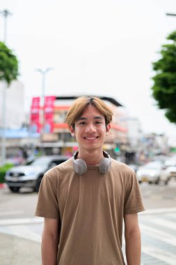 Kulaklıklı yakışıklı Asyalı genç Taylandlı yaz boyunca modern yaşam tarzının tadını çıkarıyor.