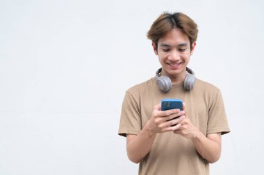 Kulaklıklı yakışıklı Asyalı genç Taylandlı beyaz arka planda modern hayat portresinin keyfini çıkarıyor.