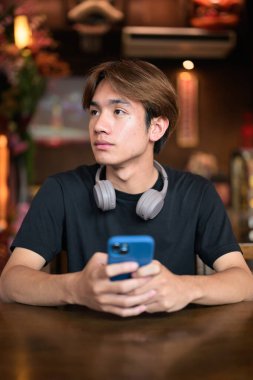 Geleneksel Çin tarzı çay restoranında telefonu sıradan tarzda kullanan Taylandlı genç bir adamın portresi. Çeşitli kavramlar ve kullanımlar için kendine güvenen, rahat ve otantik görünüm