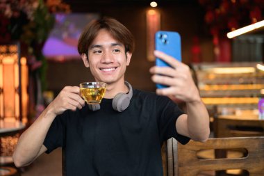 Geleneksel Çin tarzı çay restoranında telefonu sıradan tarzda kullanan Taylandlı genç bir adamın portresi. Çeşitli kavramlar ve kullanımlar için kendine güvenen, rahat ve otantik görünüm