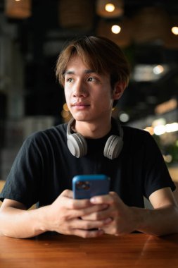 Gündüz otururken cep telefonu kullanan Taylandlı genç bir adamın portresi. Çeşitli kavramlar ve kullanımlar için kendine güvenen, rahat ve otantik görünüm