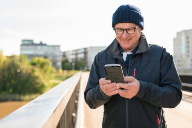 Happy senior man using mobile phone in the city. Technology concept.