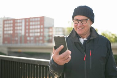 Happy senior man using mobile phone in the city. Technology concept.